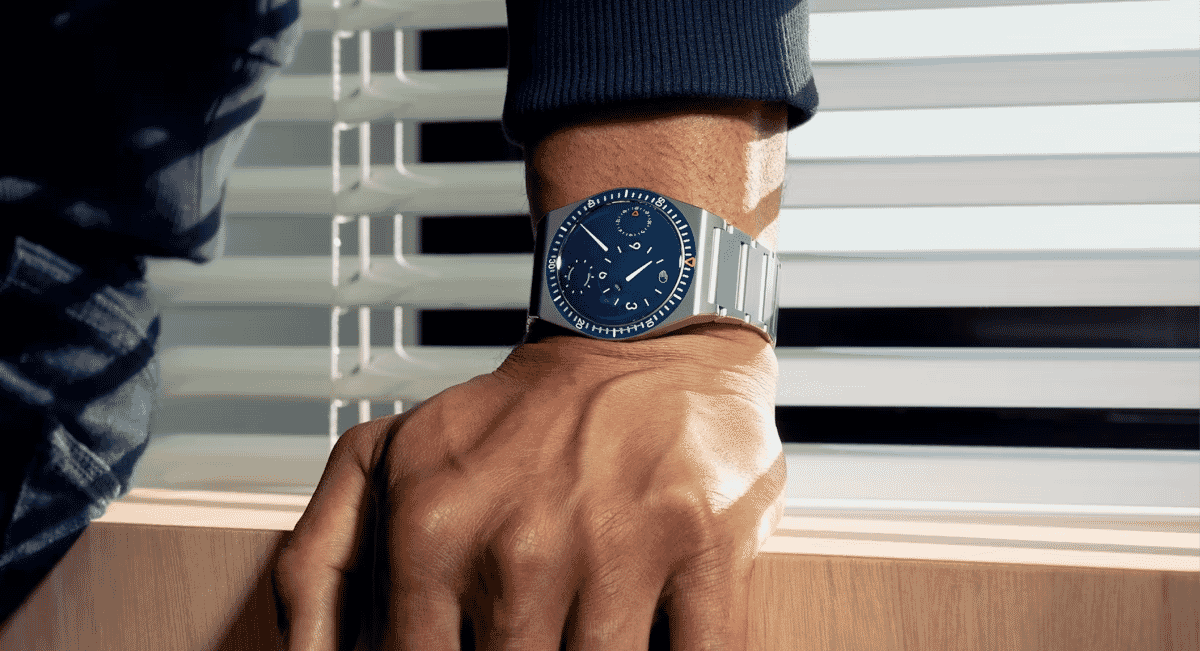 Close-up of a blue dial luxury watch worn with a dark ribbed sweater and denim jeans.