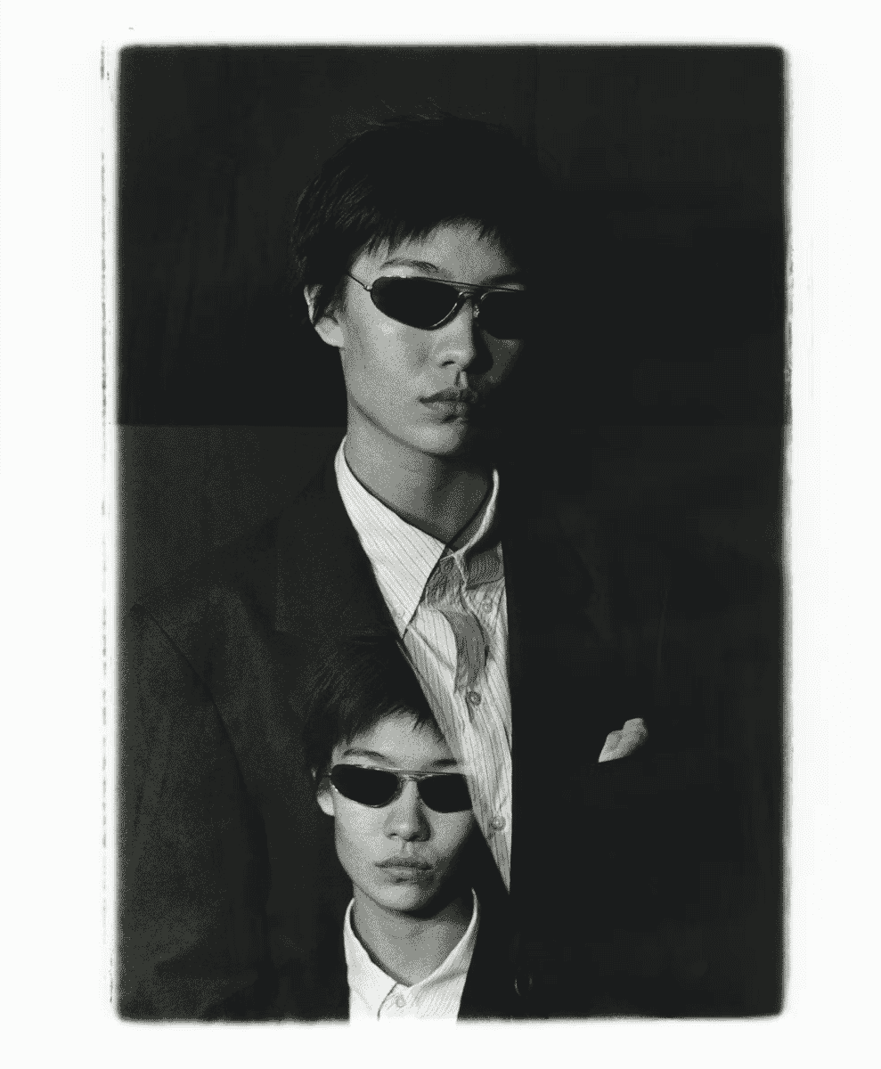Two men in sharp suits with sunglasses, posing for a high-fashion black-and-white portrait.