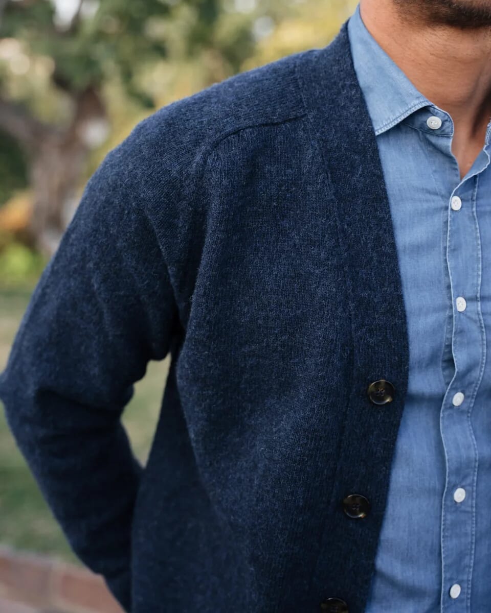 Close-up of a man in a navy blue knit cardigan over a light blue button-down shirt.