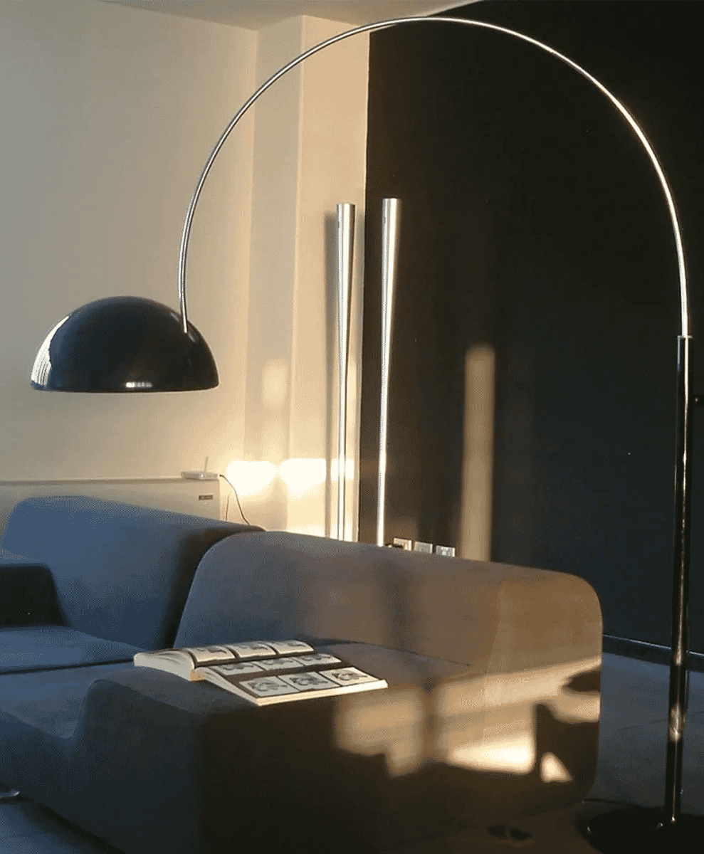 A silver arc lamp with a black dome shade in a modern living room featuring a blue sofa.