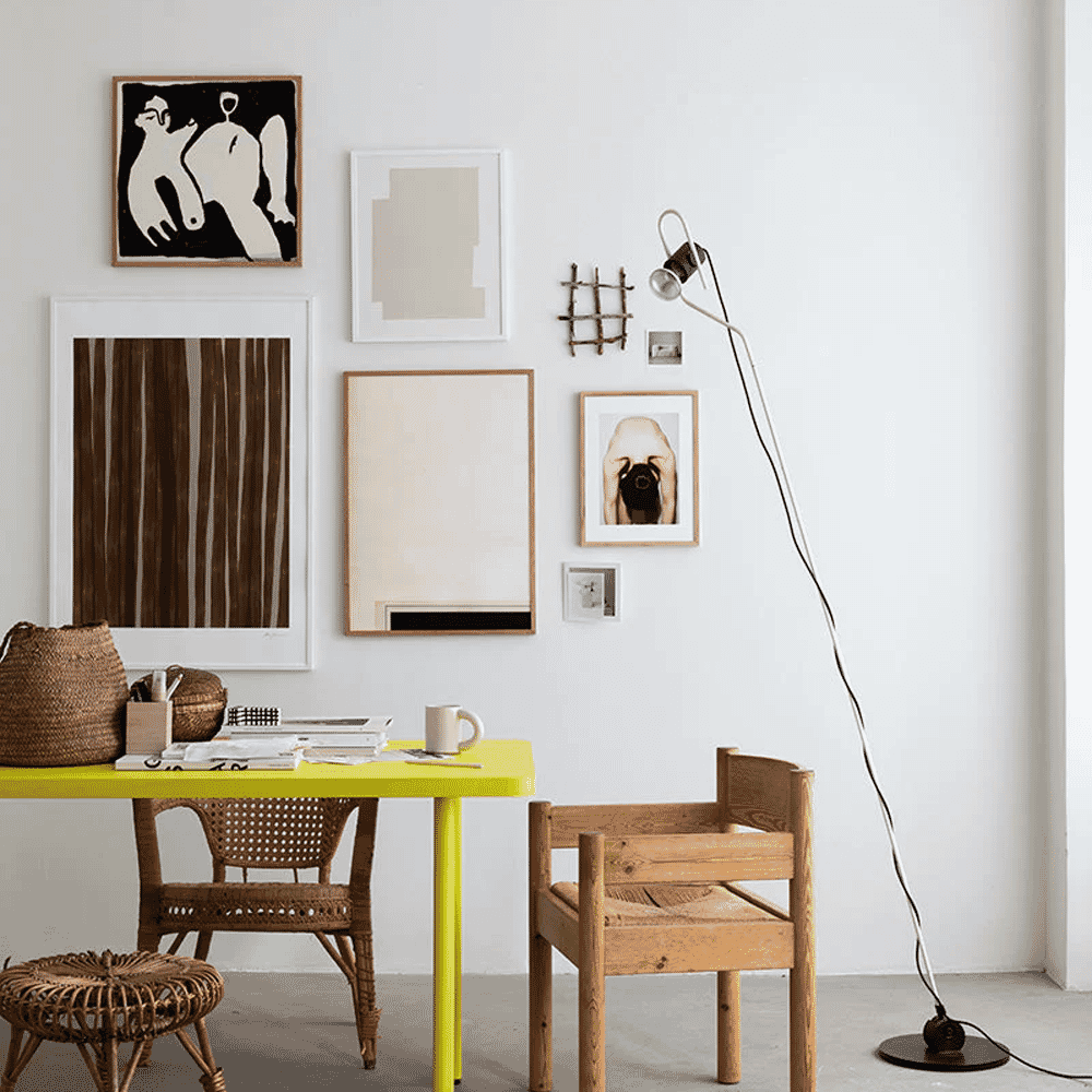 A bright yellow desk in a minimalist home office with wooden chairs and abstract wall art.
