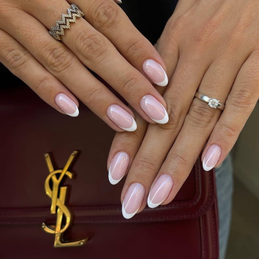 Pink French tips resting on a burgundy YSL handbag with diamond rings.