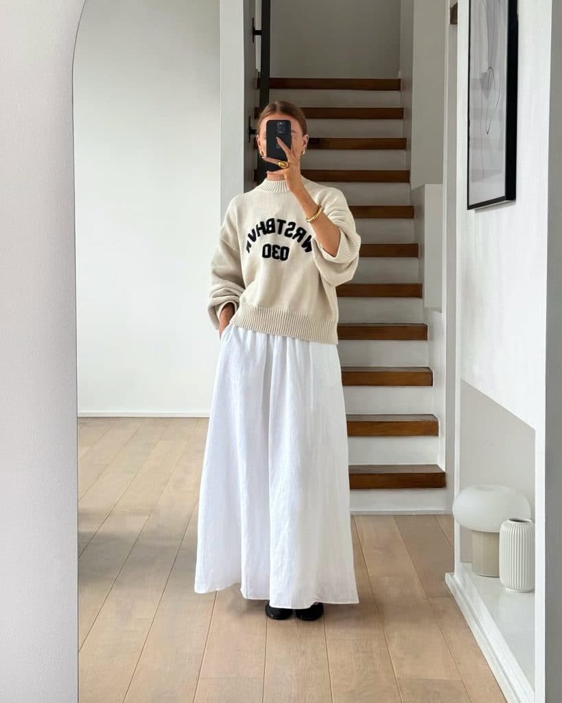 A mirror selfie of a woman in an oversized cream sweater and white maxi skirt.