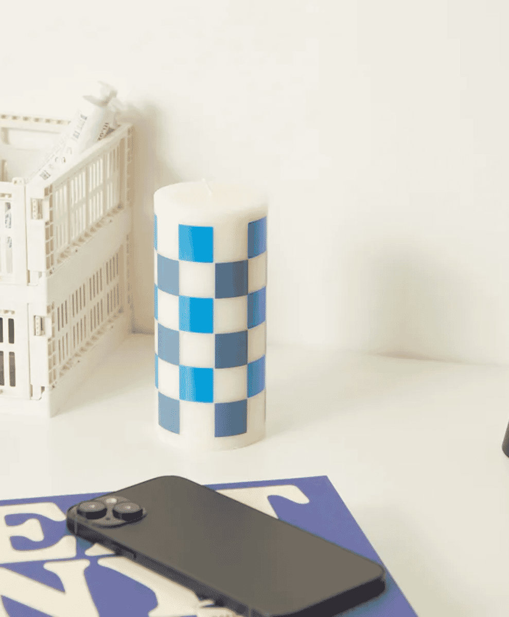 A blue and white checkered candle on a minimalist white table.