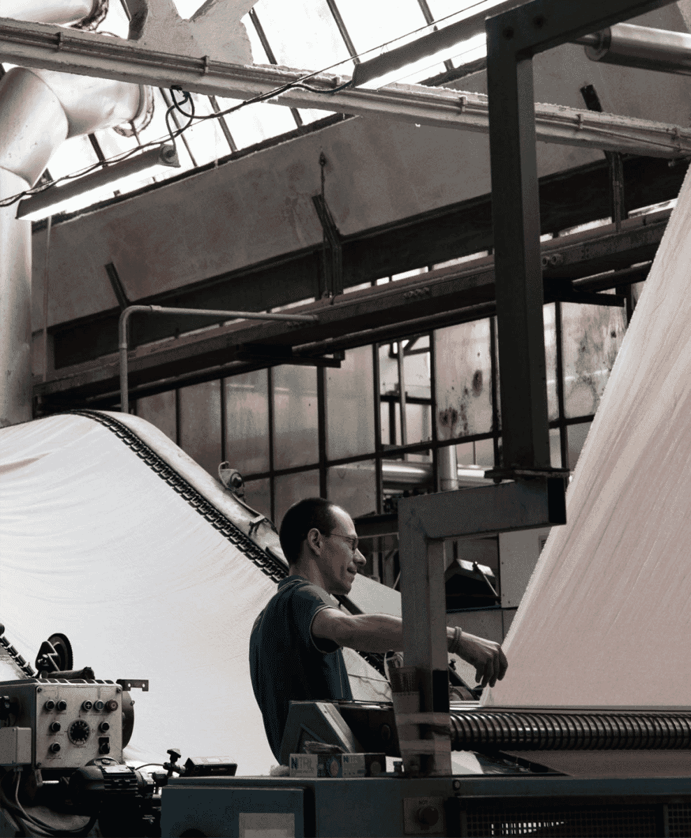 A factory worker operating textile machinery handling large rolls of fabric.