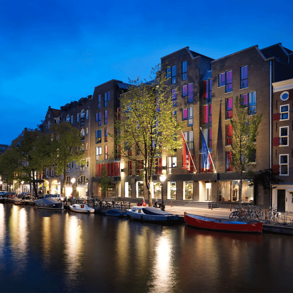 Evening view of illuminated canal-side buildings and boats in Amsterdam.