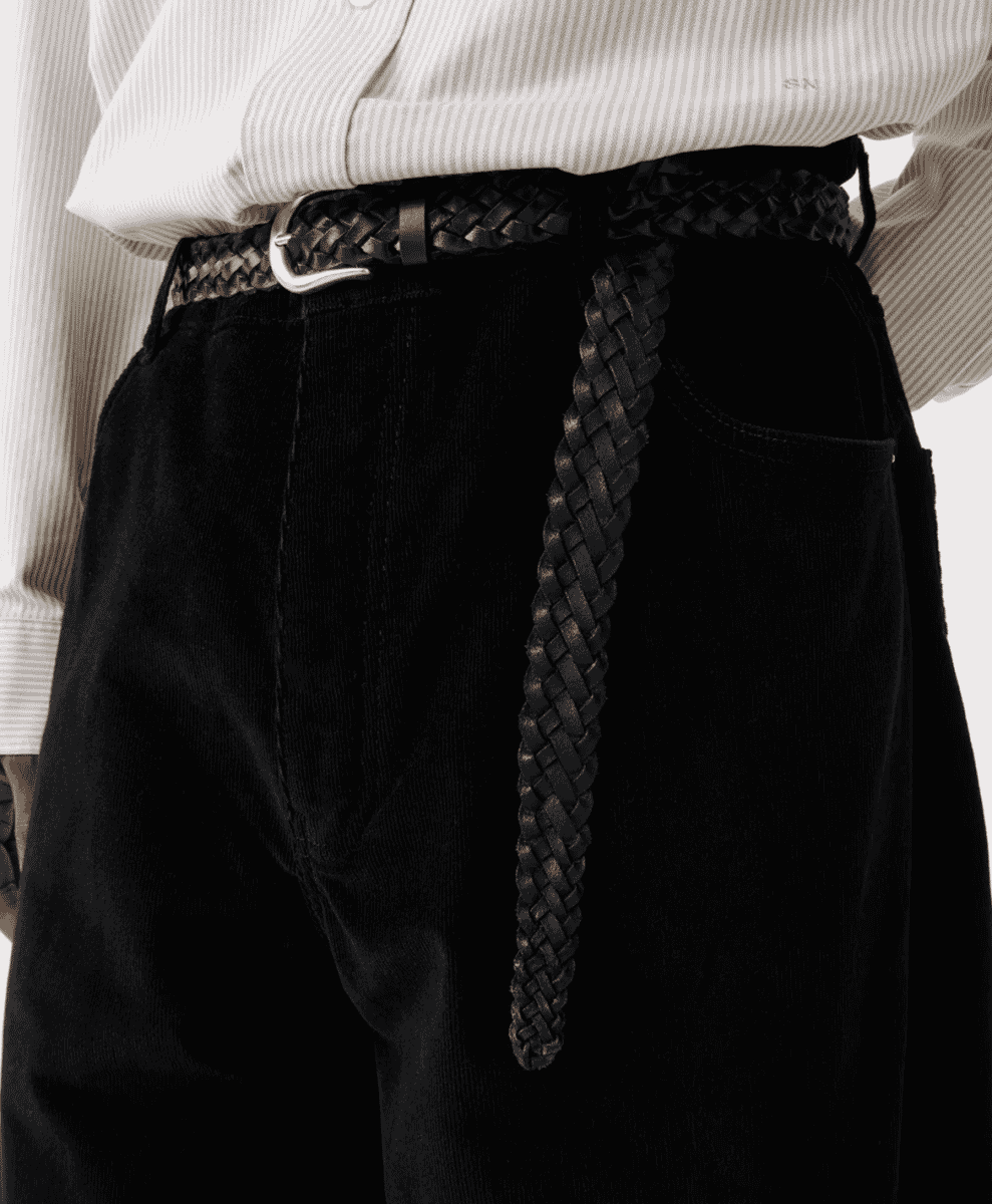 Close-up of black corduroy trousers styled with a braided leather belt and white shirt.