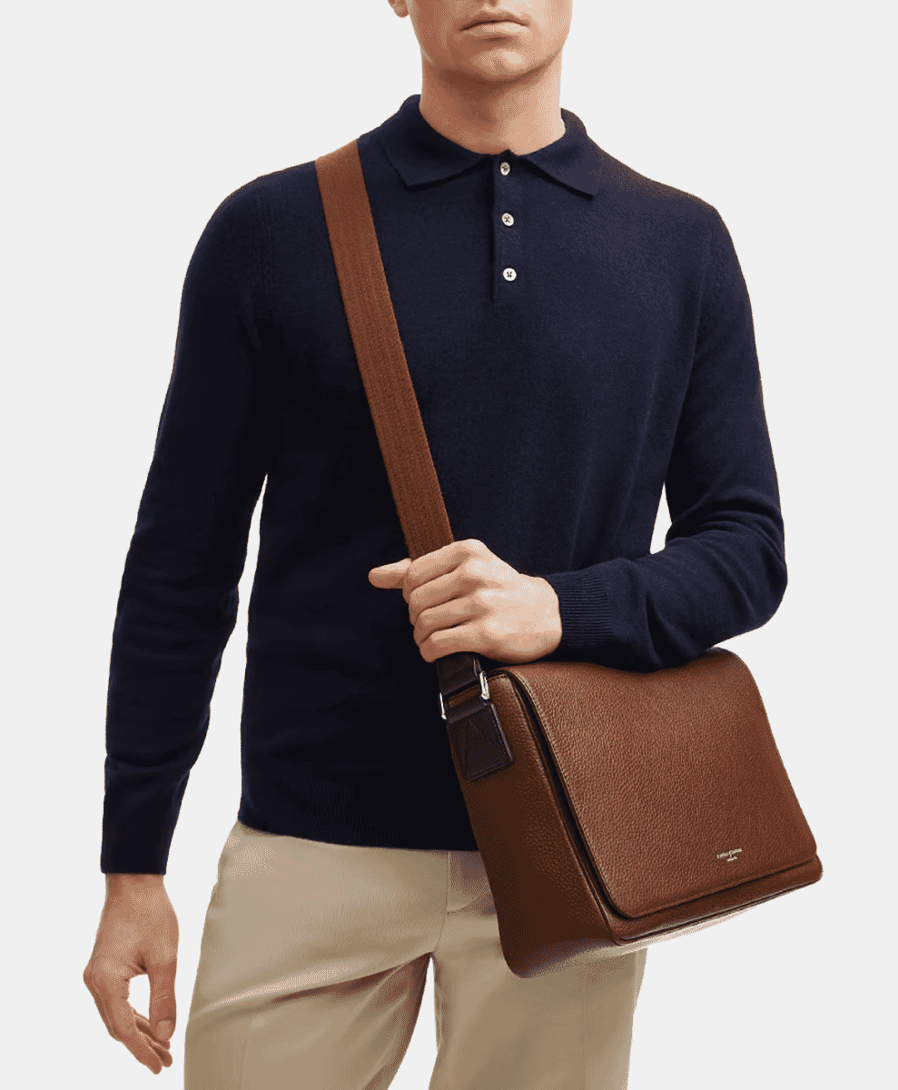 A man in a navy blue polo sweater carrying a brown leather messenger bag.