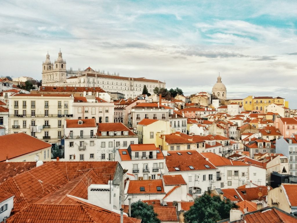 Panoramic view of Lisbon's historic district with white buildings and red-tiled roofs under a soft sky.