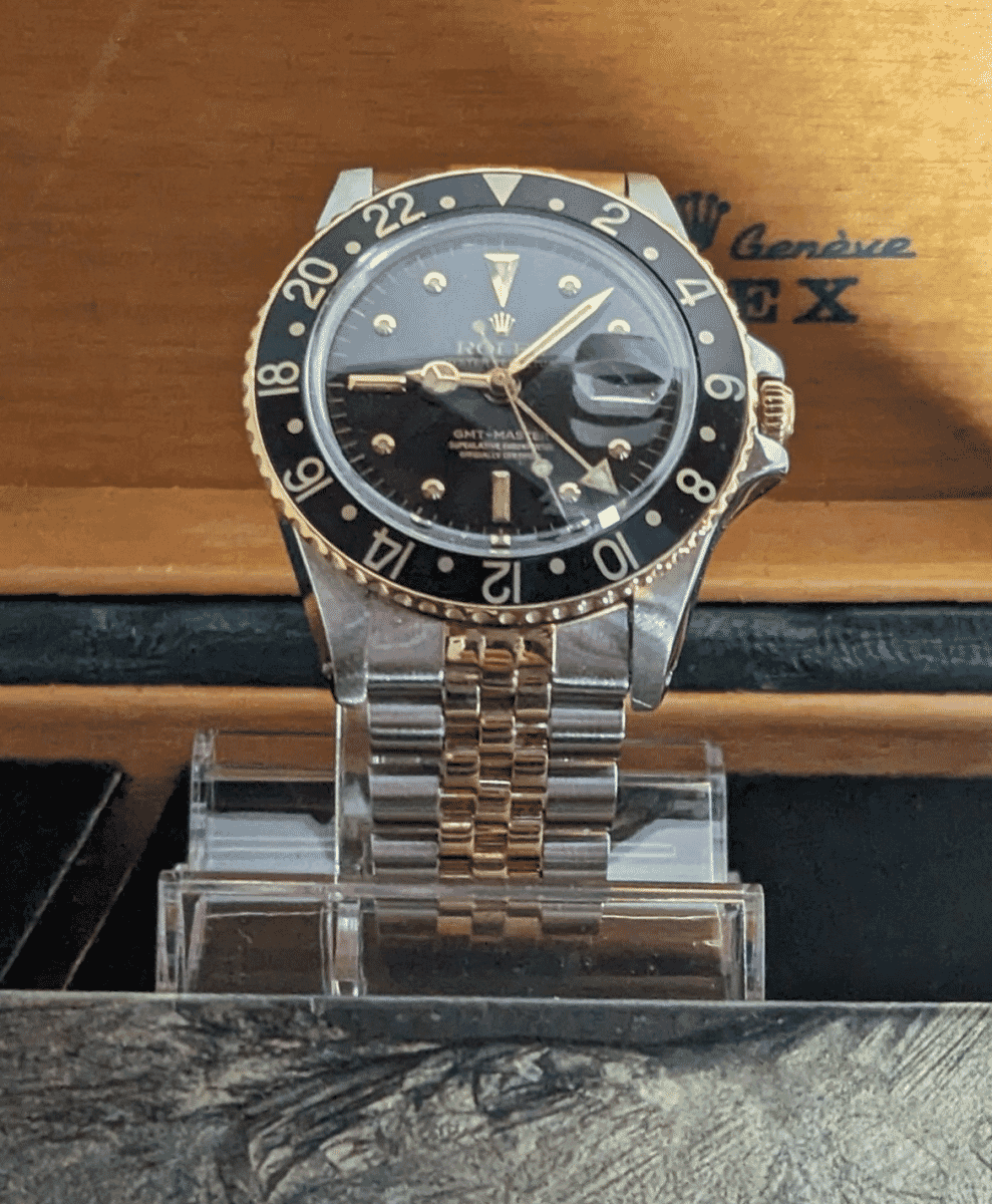 A vintage Rolex GMT-Master with a two-tone bracelet displayed inside a wooden presentation box.