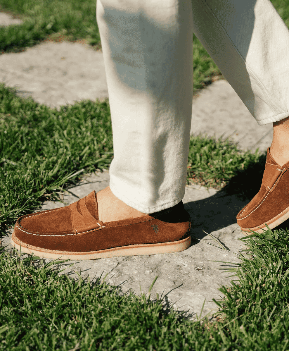 Close-up of brown suede loafers with white stitching being worn on outdoor stone steps.