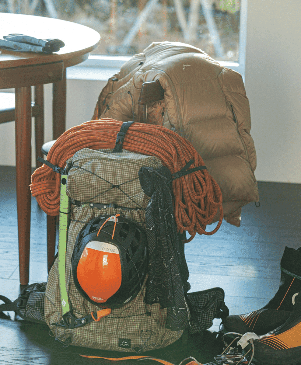 A climbing backpack with orange rope and a helmet sitting next to a puffer jacket indoors