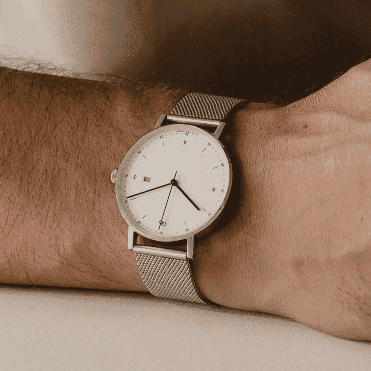 Close-up of a minimalist silver mesh-band watch with a white dial on a man's wrist.