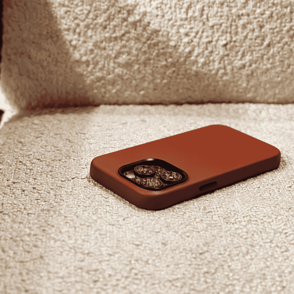 A brown matte phone case with a triple-camera cutout resting on a beige fabric surface.