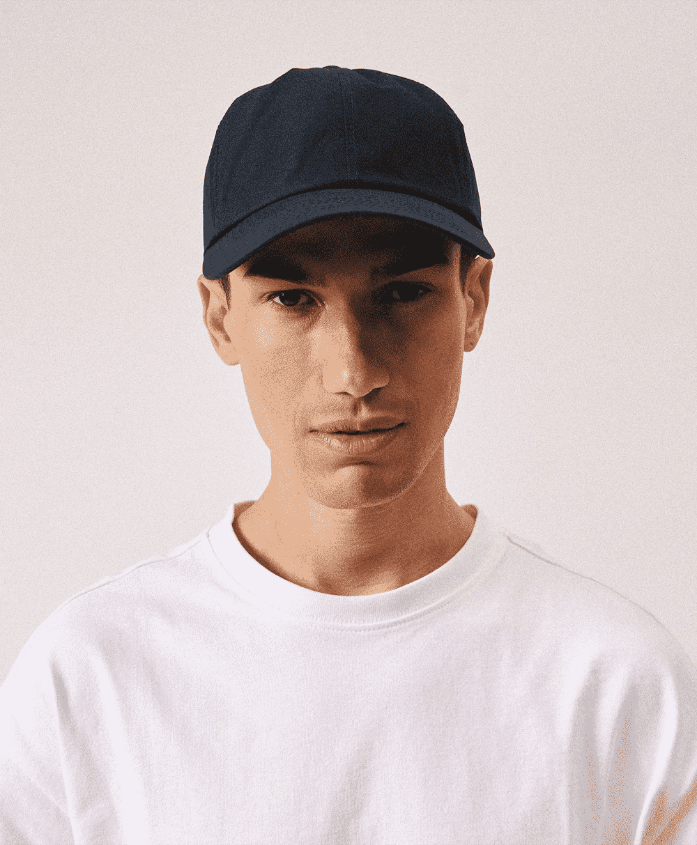 A man in a navy blue baseball cap and plain white crewneck t-shirt posing against a neutral background.
