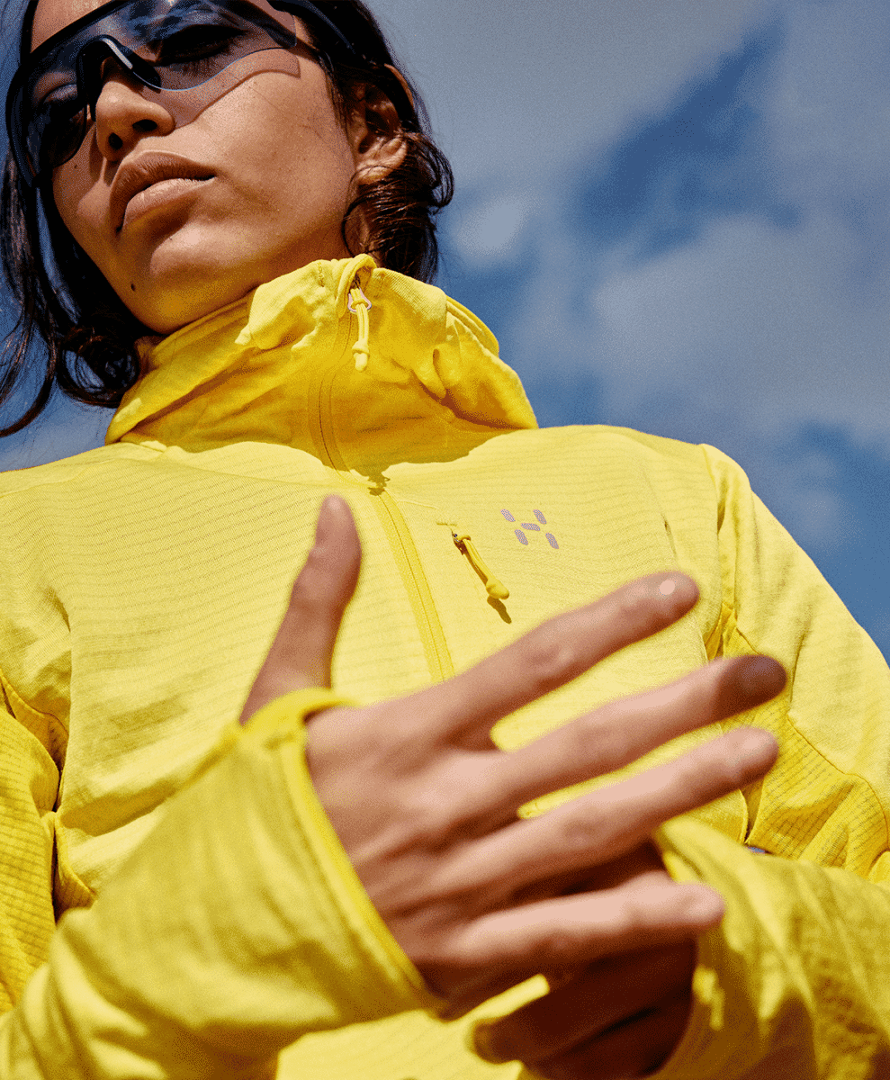 A person wearing a vibrant yellow hooded outdoor jacket and sunglasses against a clear blue sky.