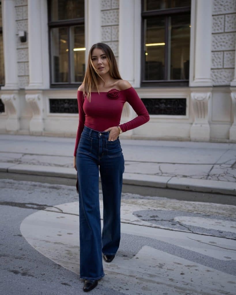 Woman wearing a burgundy off-the-shoulder top with floral detail and high-waisted wide-leg jeans.