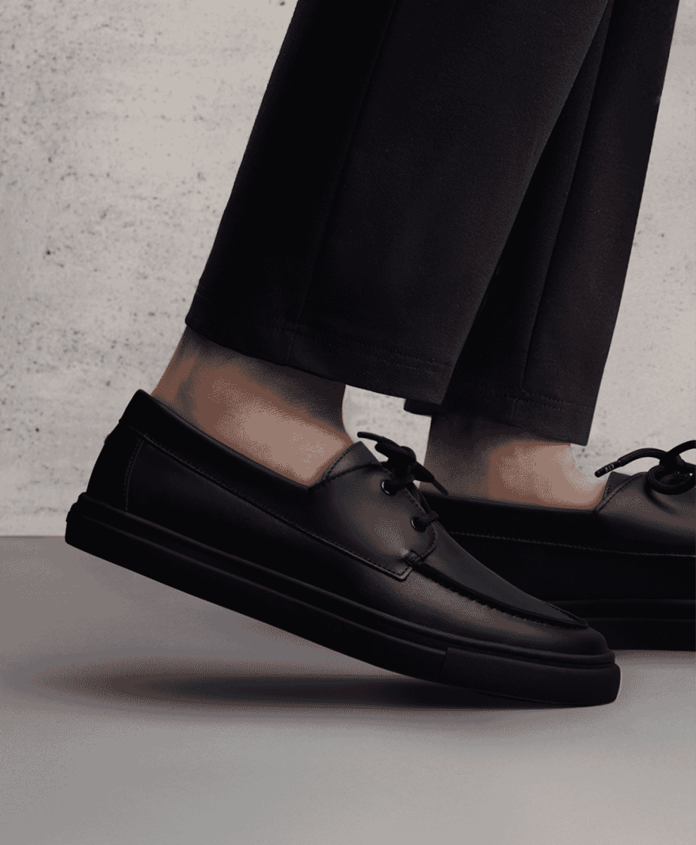 Sleek black leather DS 03 shoes paired with dark trousers on a concrete background.