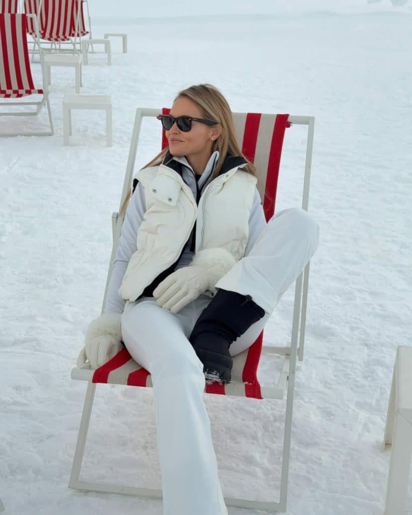 Woman lounging in a white ski vest and large sunglasses.