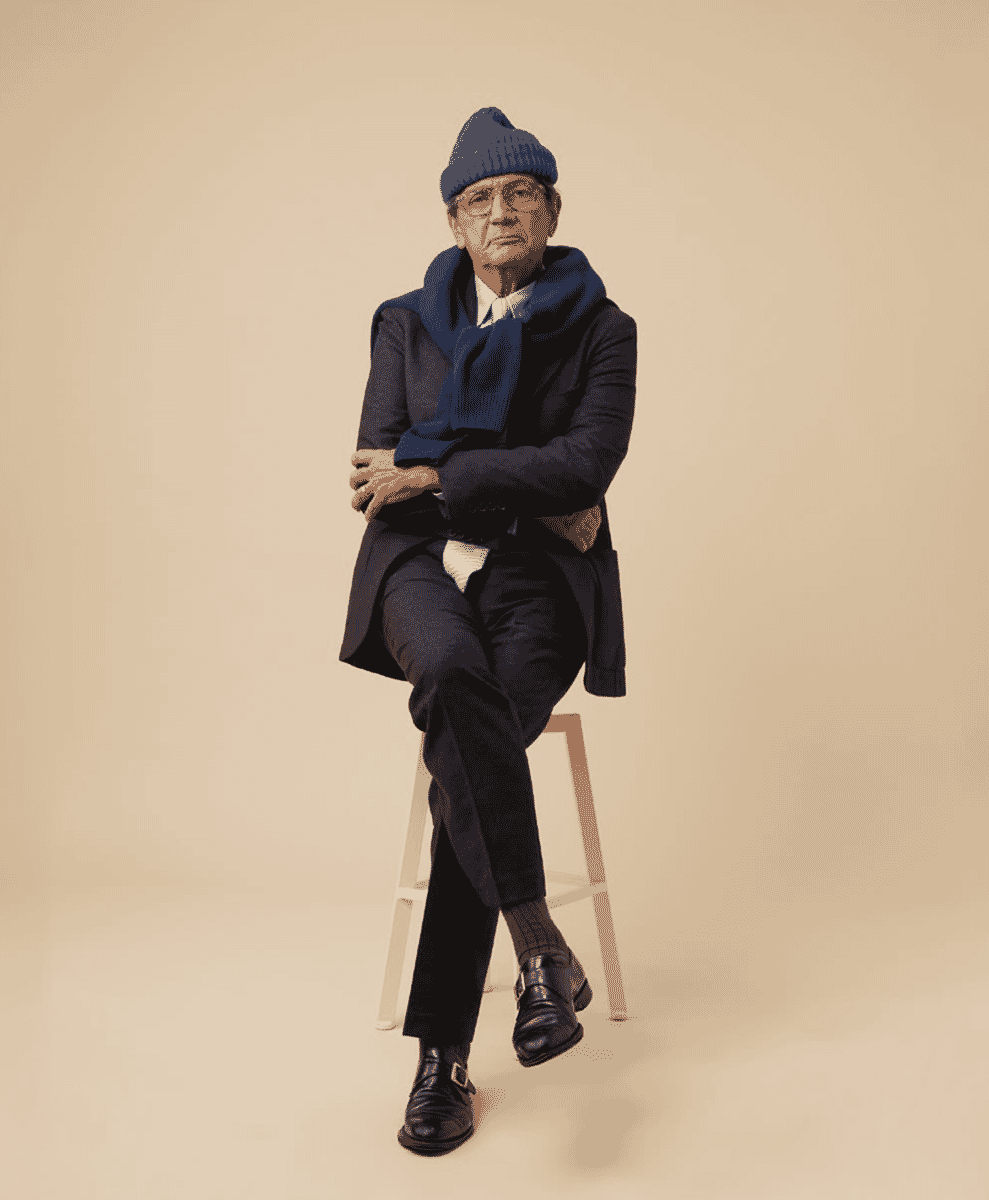 An older man wearing a navy blue beanie, matching scarf, and dark overcoat.