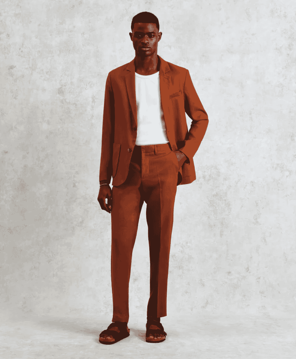 Man wearing a brown suit with casual sandals against a studio background.