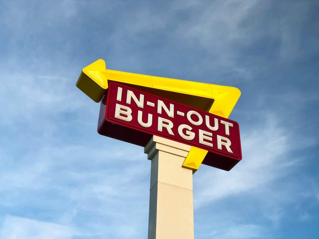 The red and yellow In-N-Out Burger sign pointing upward against a clear blue sky.