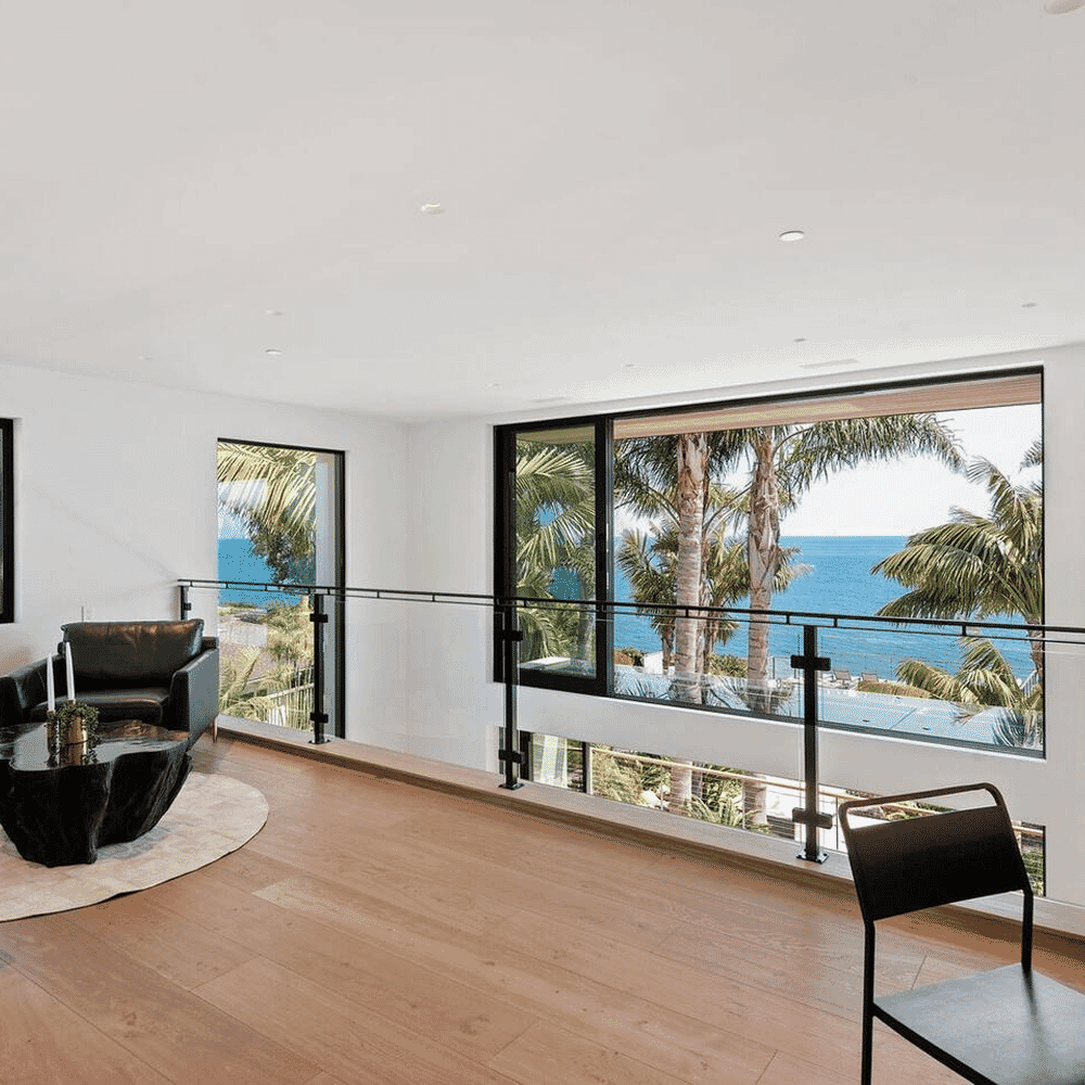 A modern minimalist living space with sleek black furniture and large windows overlooking palm trees.