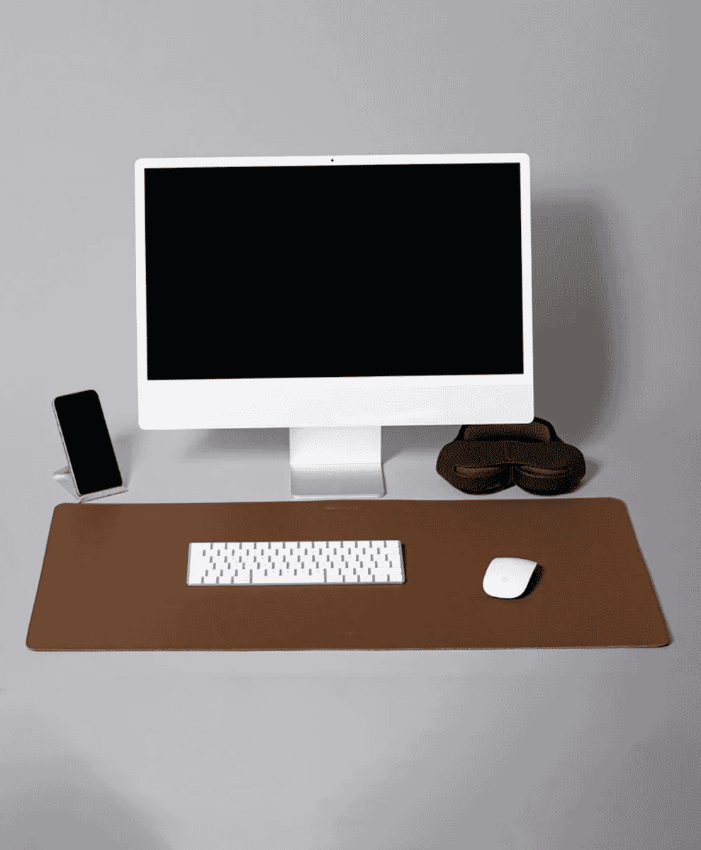 A minimalist workspace featuring a brown leather desk mat under a white iMac, keyboard, and mouse.