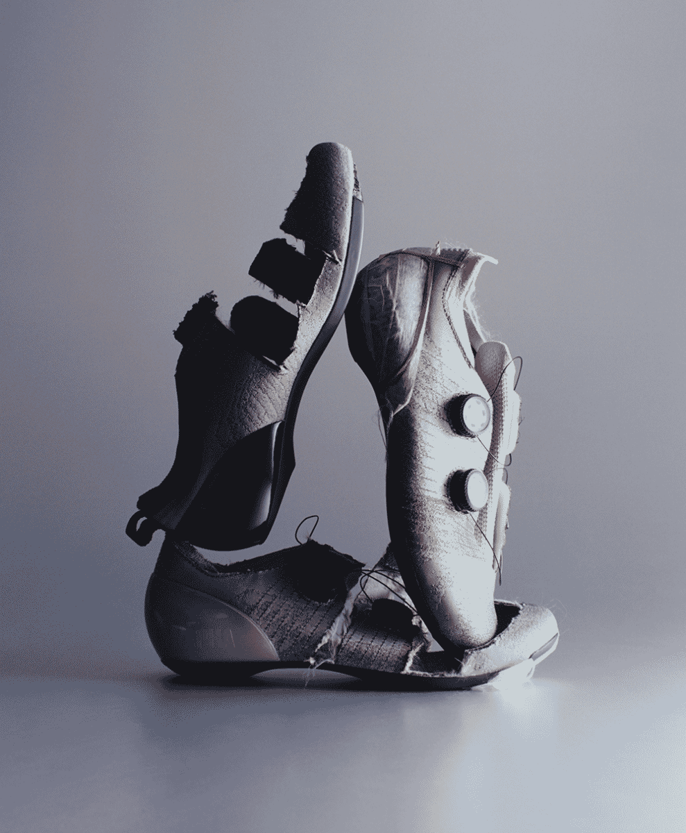 Monochrome shot of a severely damaged and torn cycling shoe showing frayed knit and structural failure.