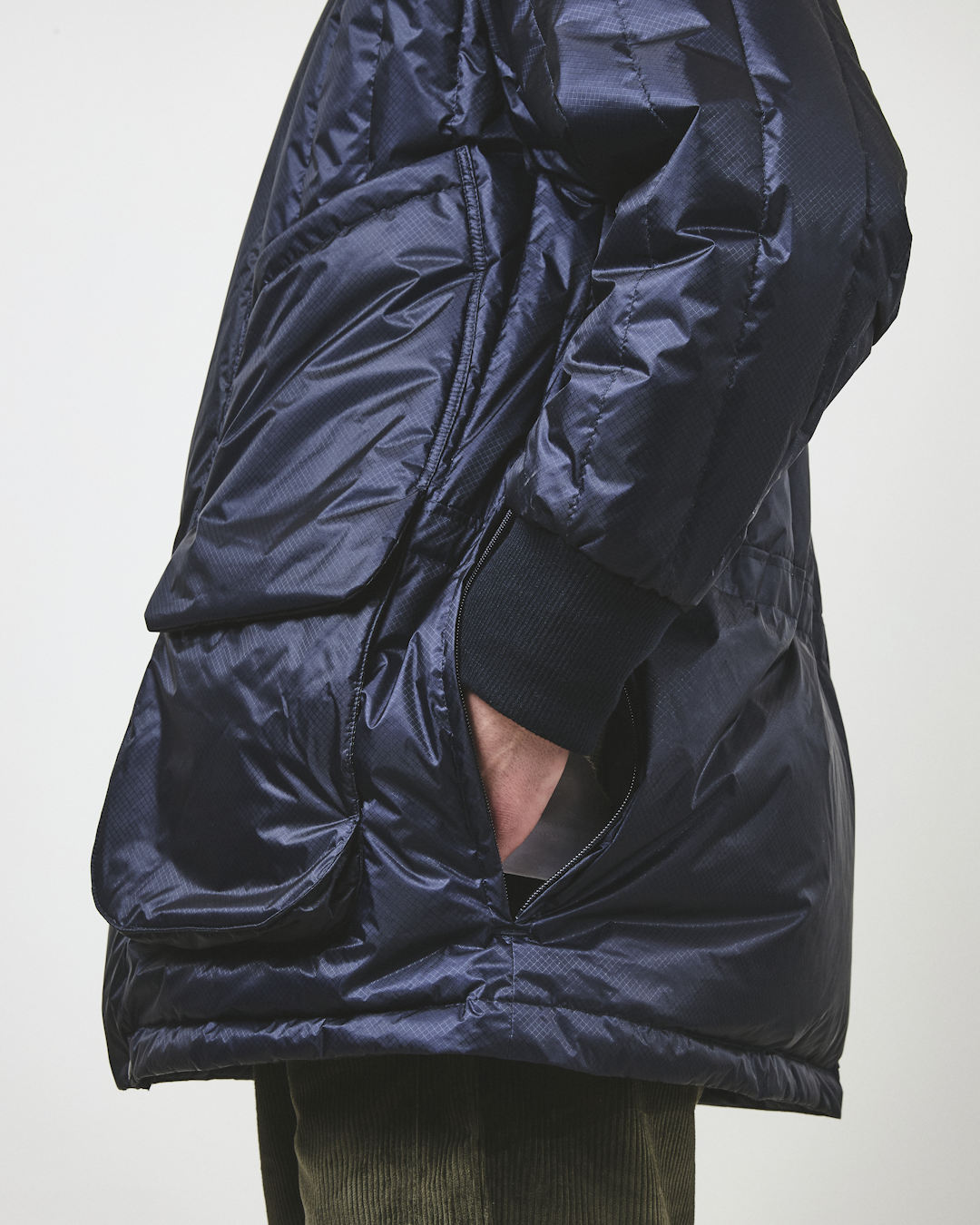 Close-up of a navy quilted puffer coat featuring large front pockets and ribbed cuffs.