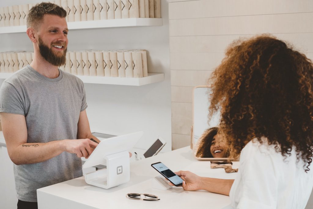 A man and woman at a retail counter using a tablet and smartphone for a digital payment transaction.