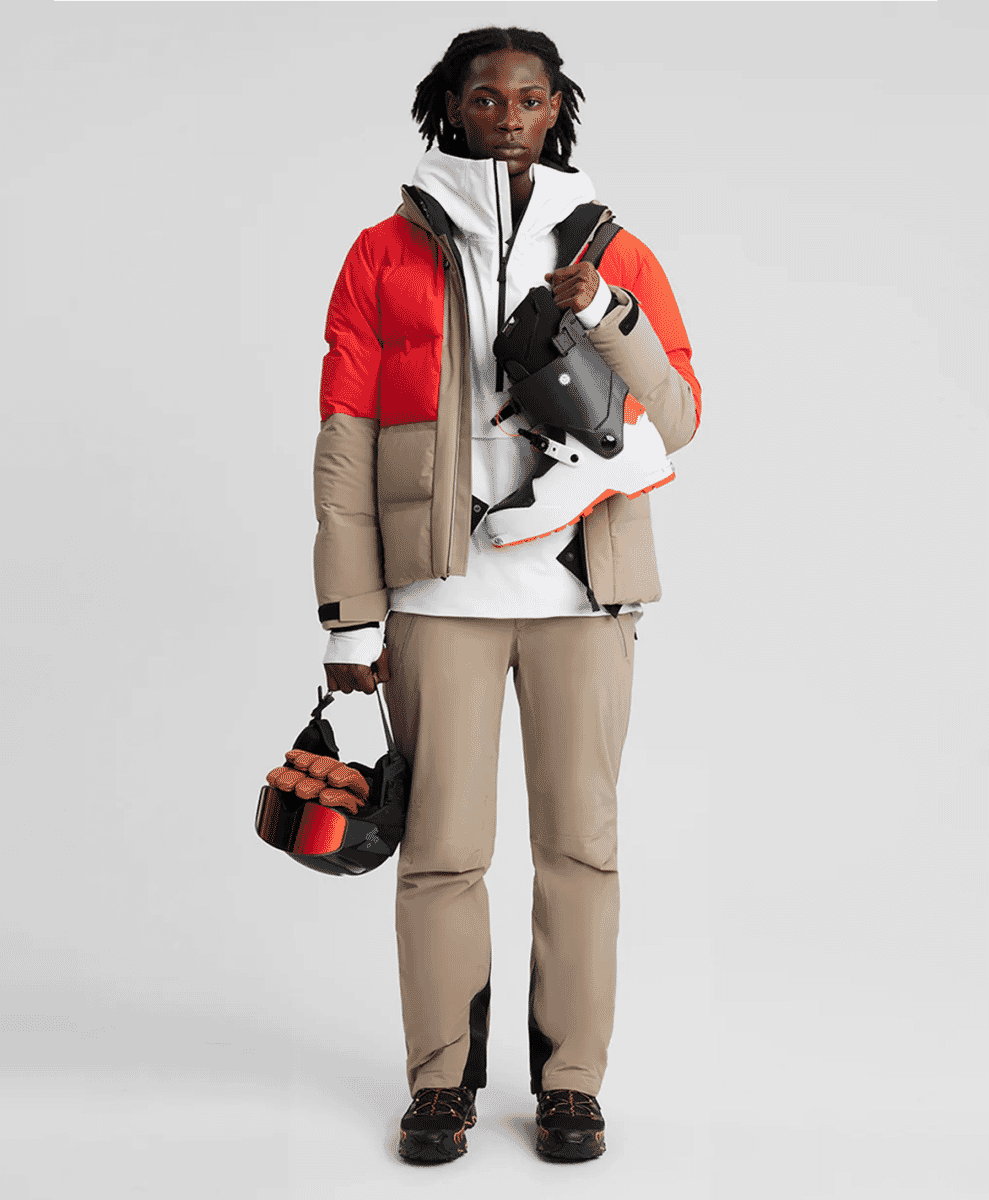 A model in a bold red, beige, and white color-blocked puffer jacket and ski pants.