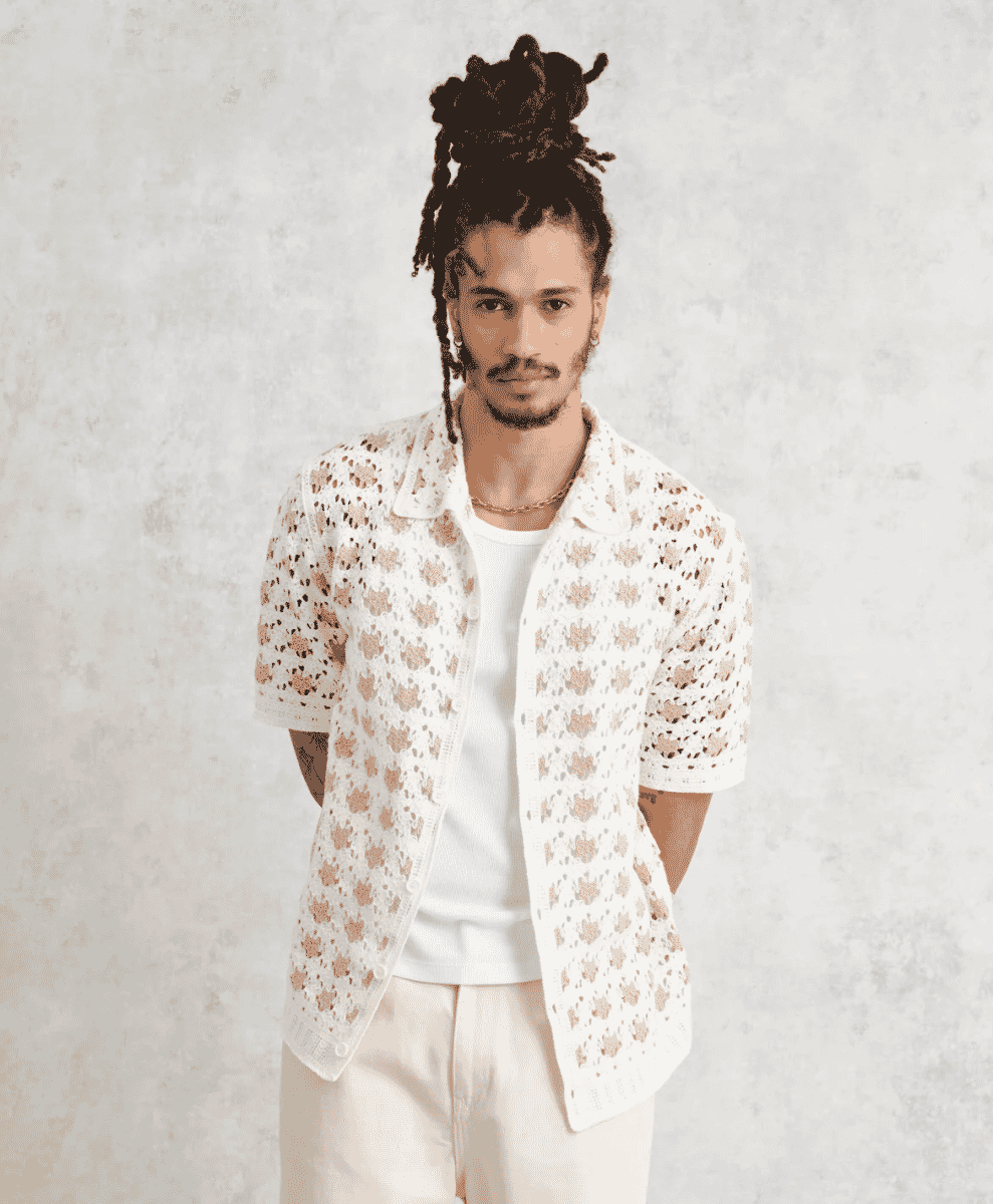 A man wears a white short-sleeved knitted shirt with floral lace patterns.