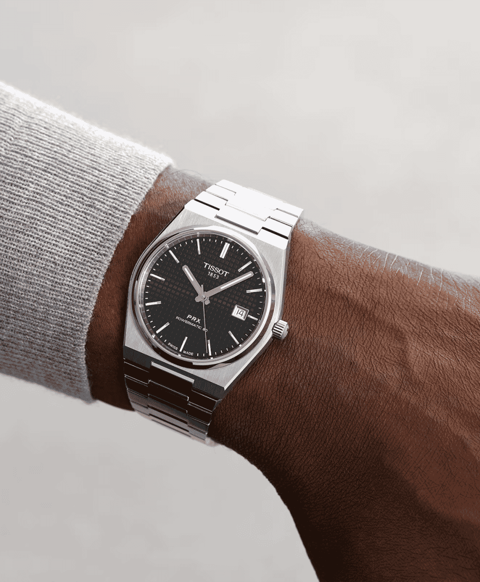 Wrist shot of a Tissot PRX watch paired with a light grey ribbed sweater.