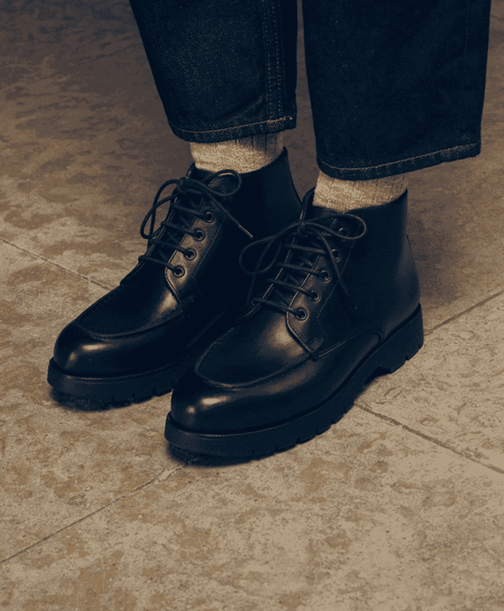 Black leather boots paired with dark denim and visible light-colored socks on a tiled floor.