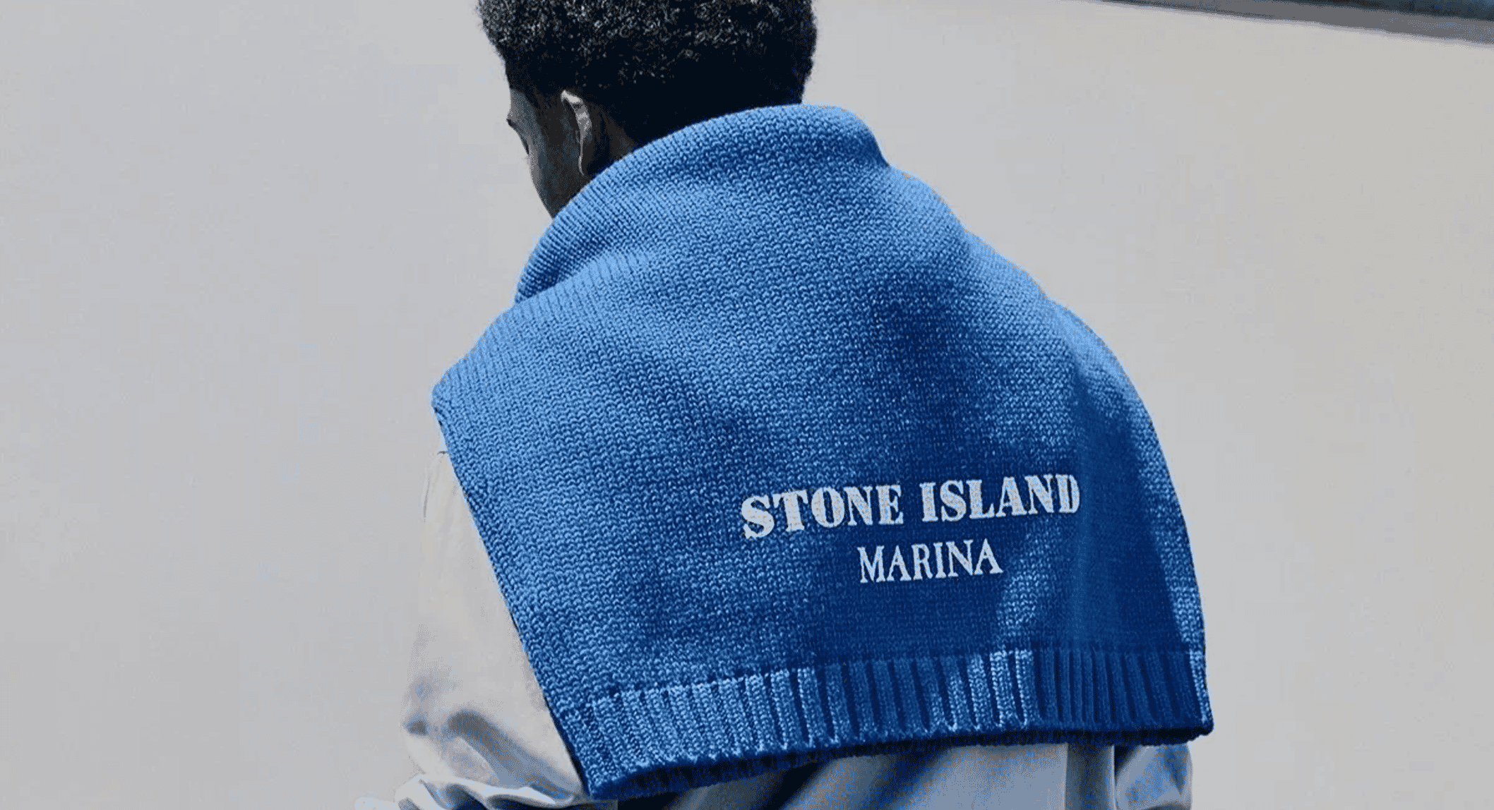 A person viewed from behind wearing a blue knitted vest with 'STONE ISLAND MARINA' white embroidery.