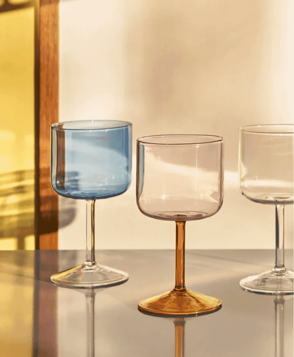 Amber and blue tinted wine glasses on a reflective surface in warm light.