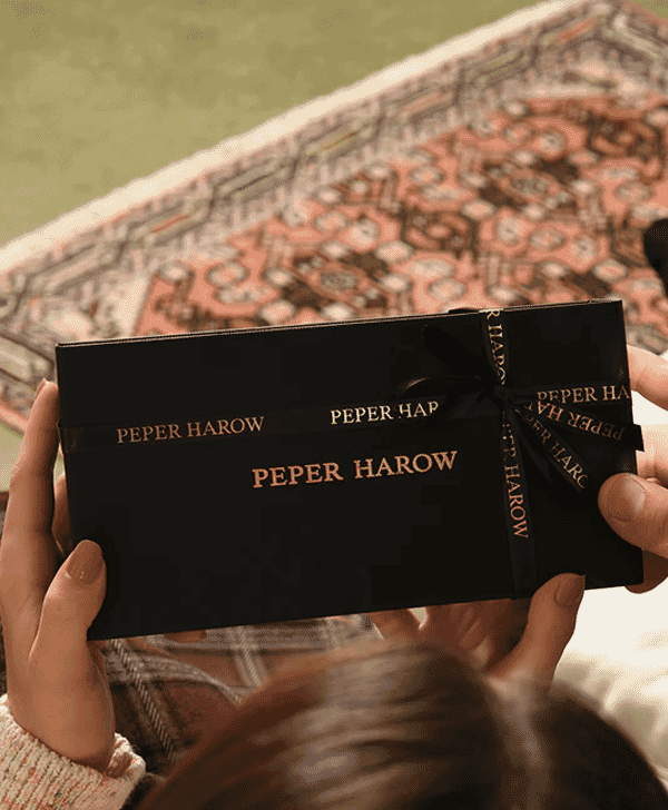 A person holding a black Peper Harow gift box with gold lettering.