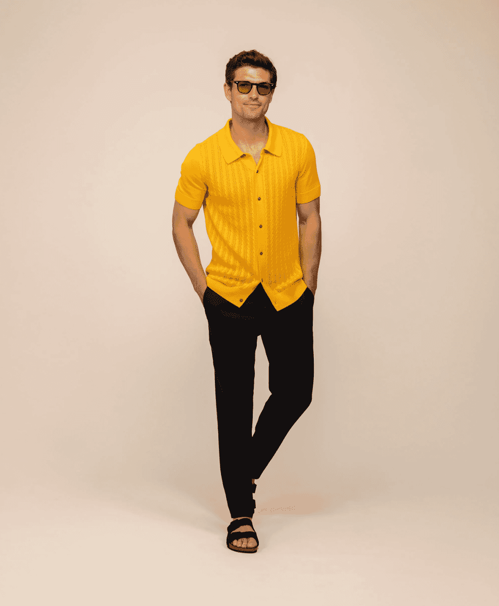 Man in yellow cable-knit button-up shirt and black trousers with sunglasses