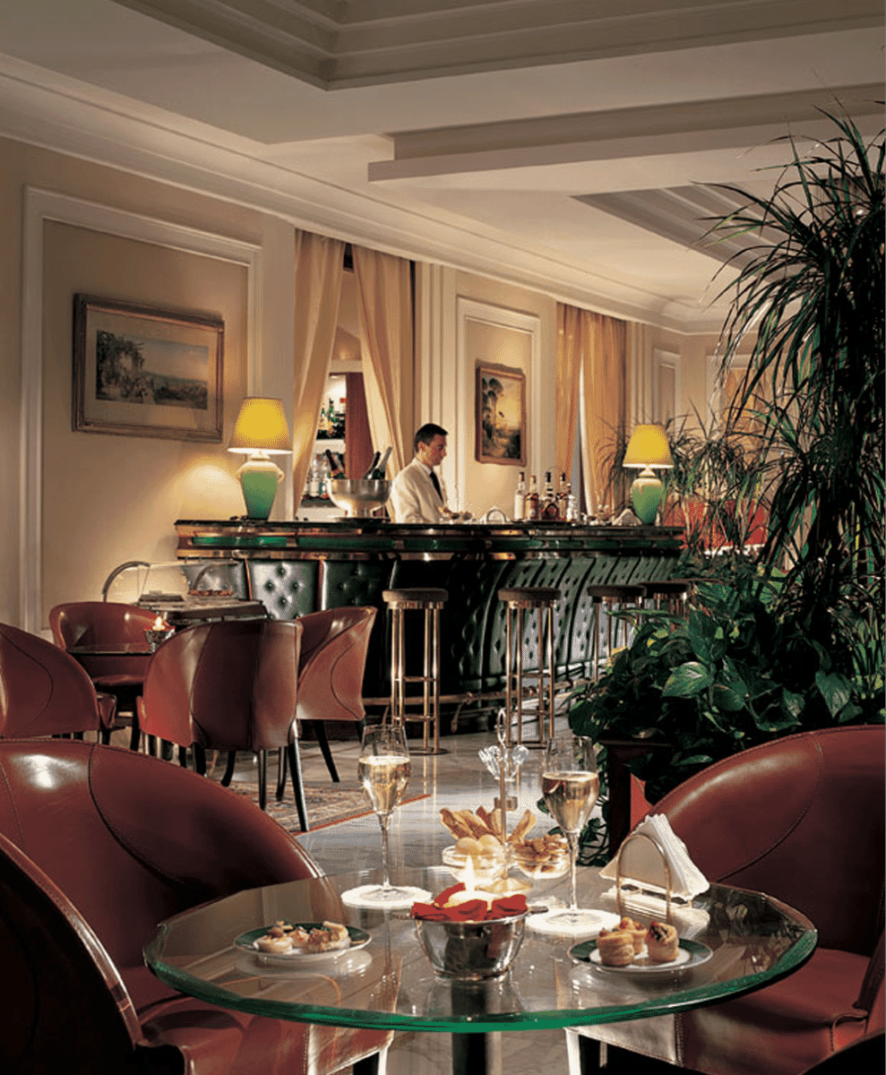 A bartender in formal attire preparing drinks at an elegant, dimly lit luxury bar.