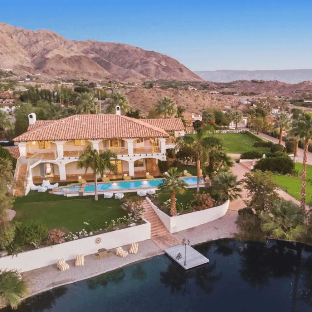 Luxury villa estate with a swimming pool and palm trees set against desert mountains.