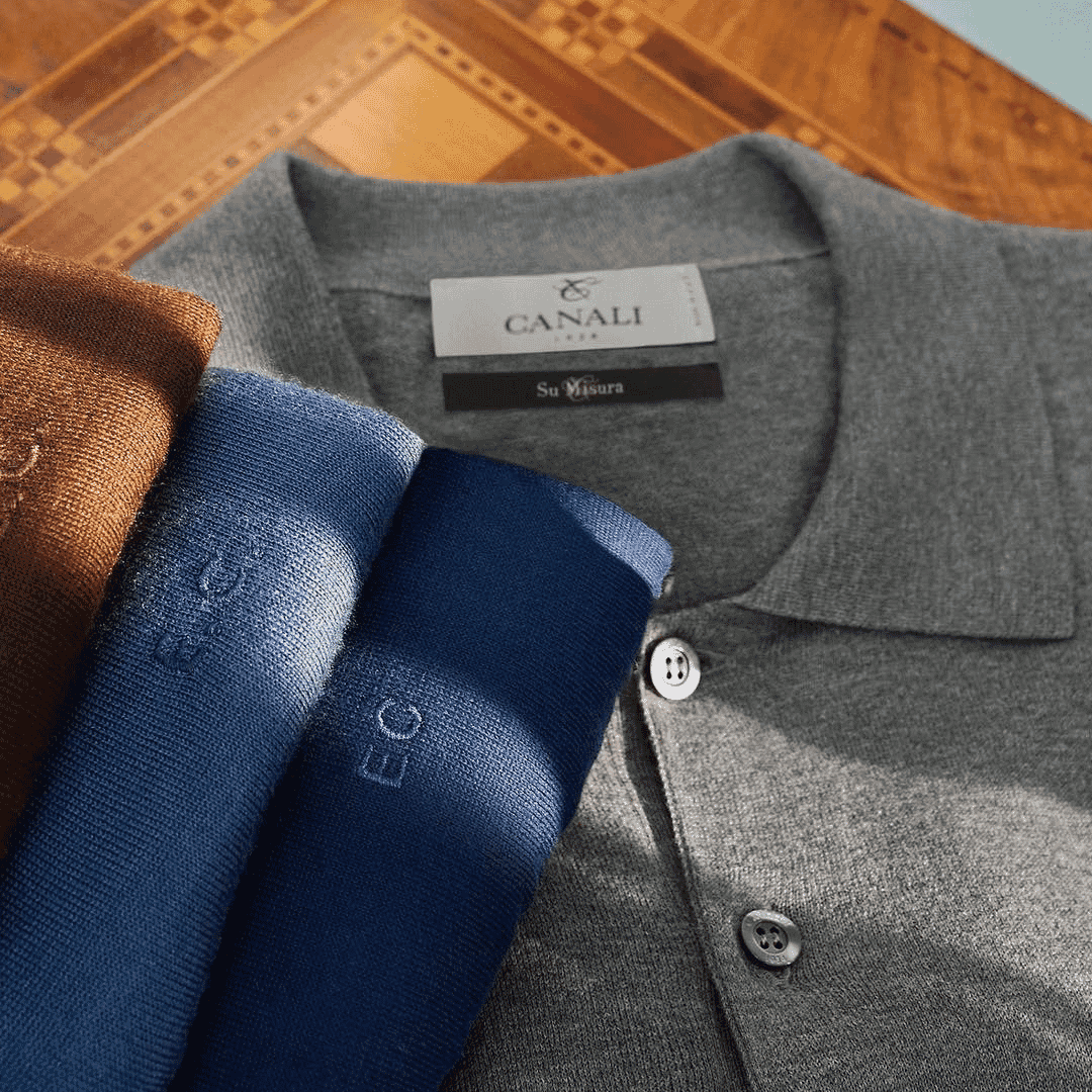 Close-up of a grey Canali polo shirt with the 'Su Misura' label alongside folded luxury knitwear.