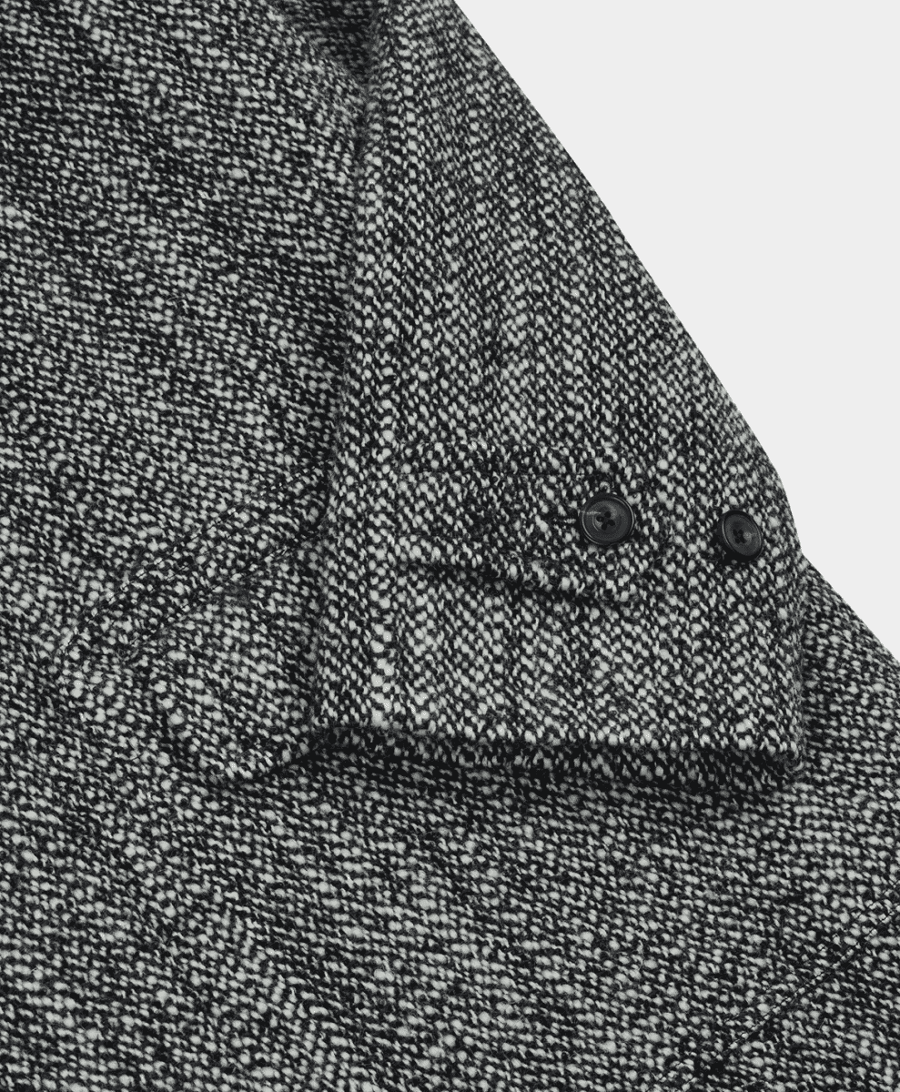 Close-up of a herringbone wool coat sleeve showing button details and fabric weave.