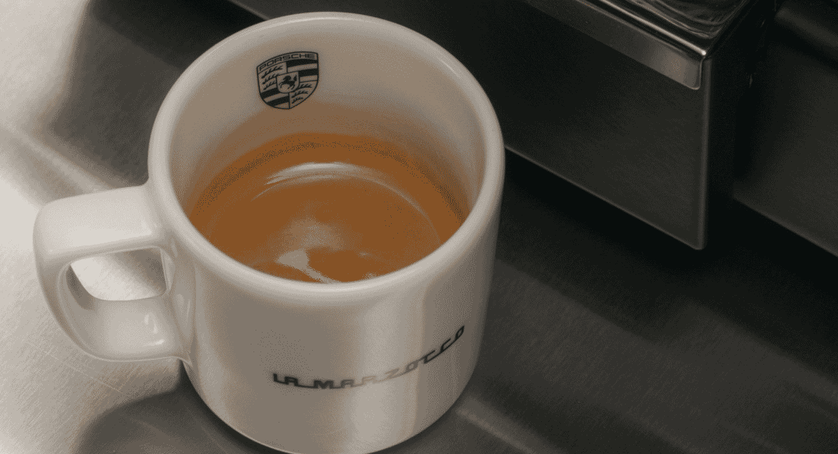 A white ceramic Porsche x La Marzocco coffee mug filled with espresso.
