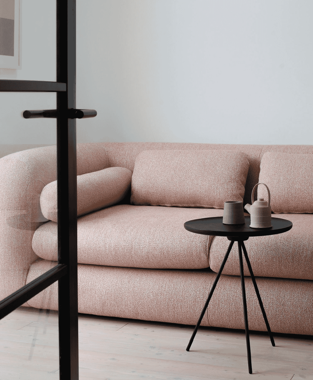 Plush pink sofa with a black side table and a ceramic tea set on light wood flooring.