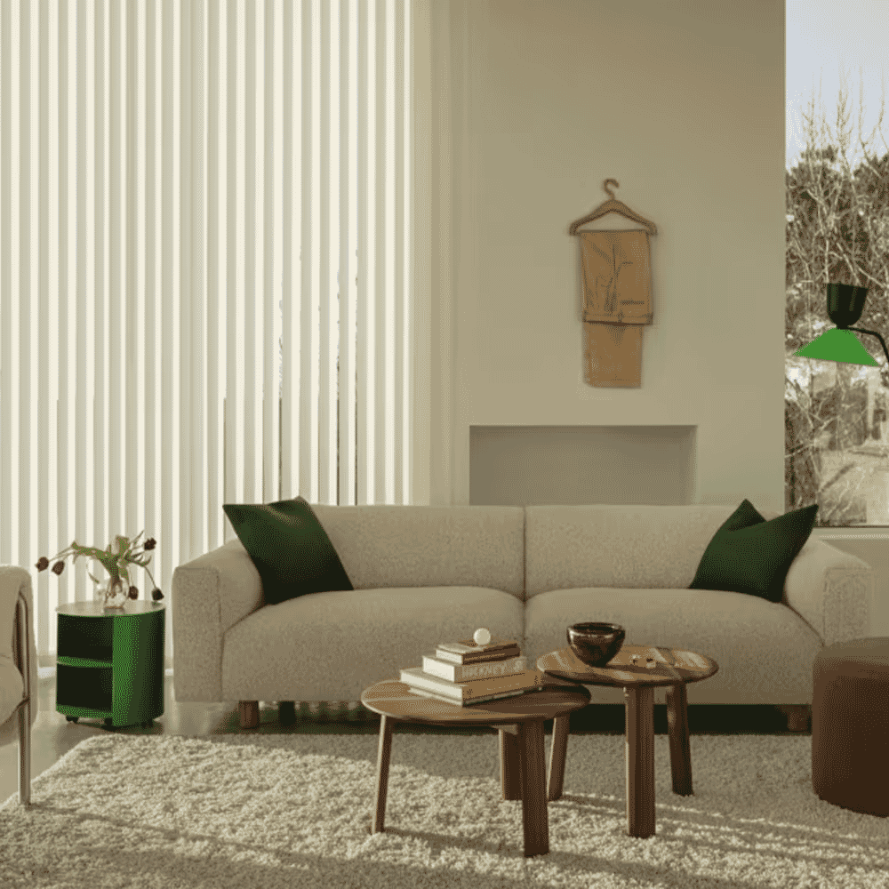Minimalist living room featuring a beige sofa styled with dark green pillows and wooden coffee tables.