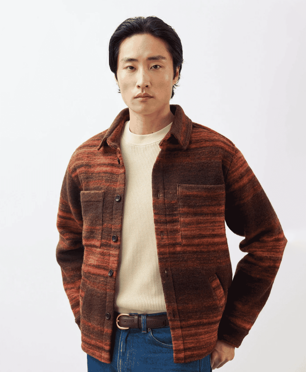 Man modeling a rust-colored striped wool overshirt over a cream waffle-knit sweater.