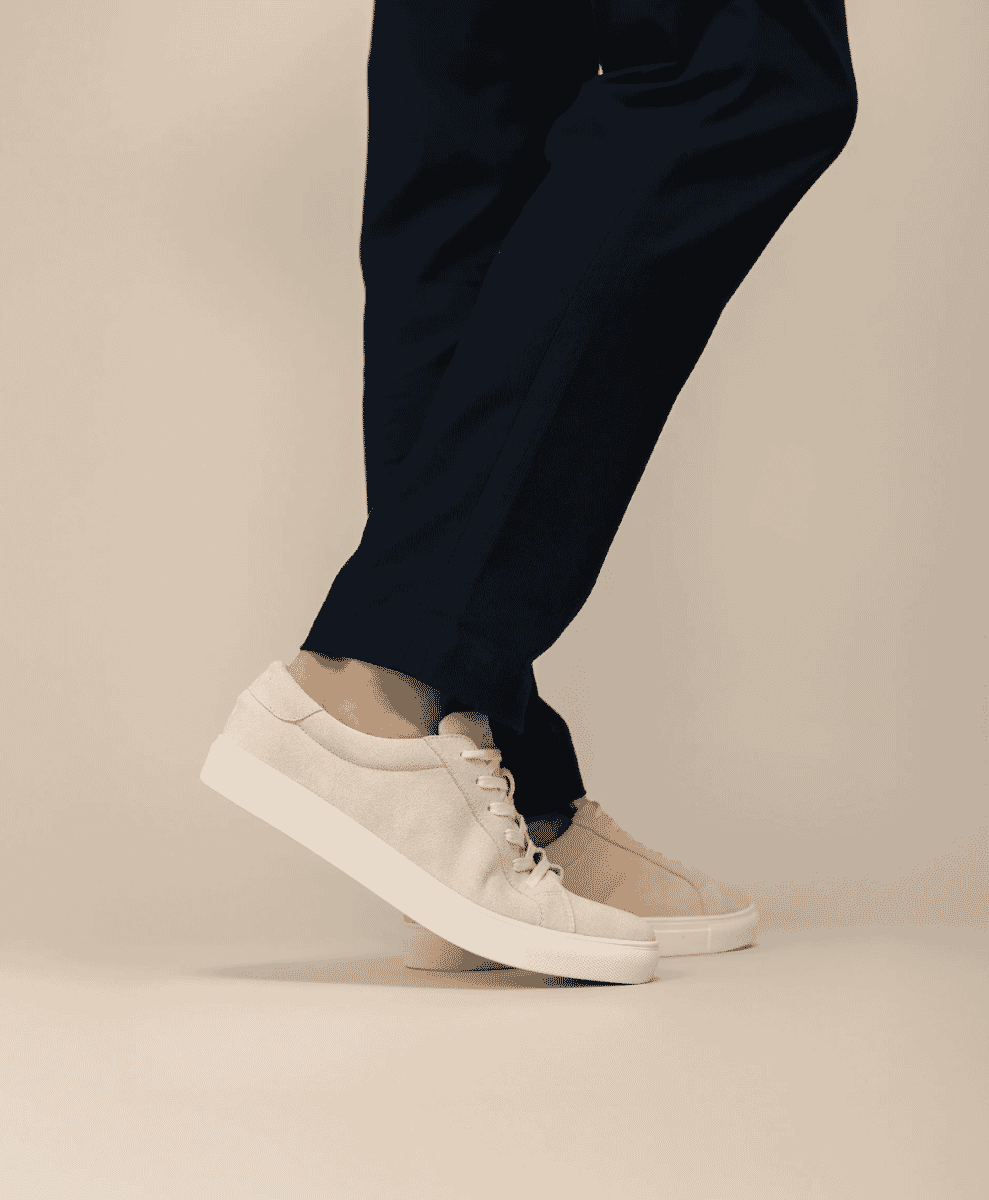 A person wearing minimalist white suede sneakers with navy trousers.