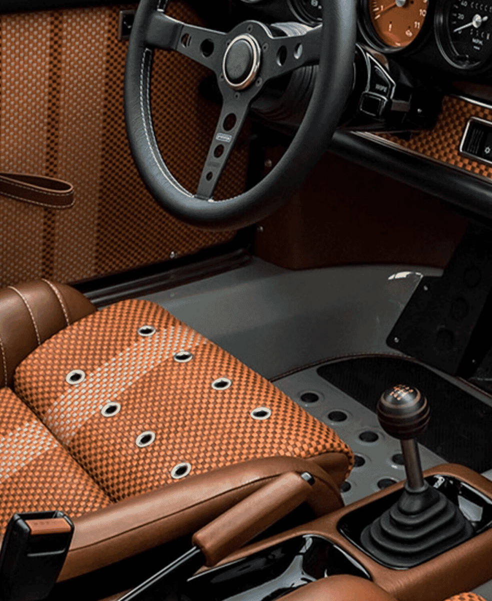 Vintage car interior with orange perforated leather seats and a classic black steering wheel.