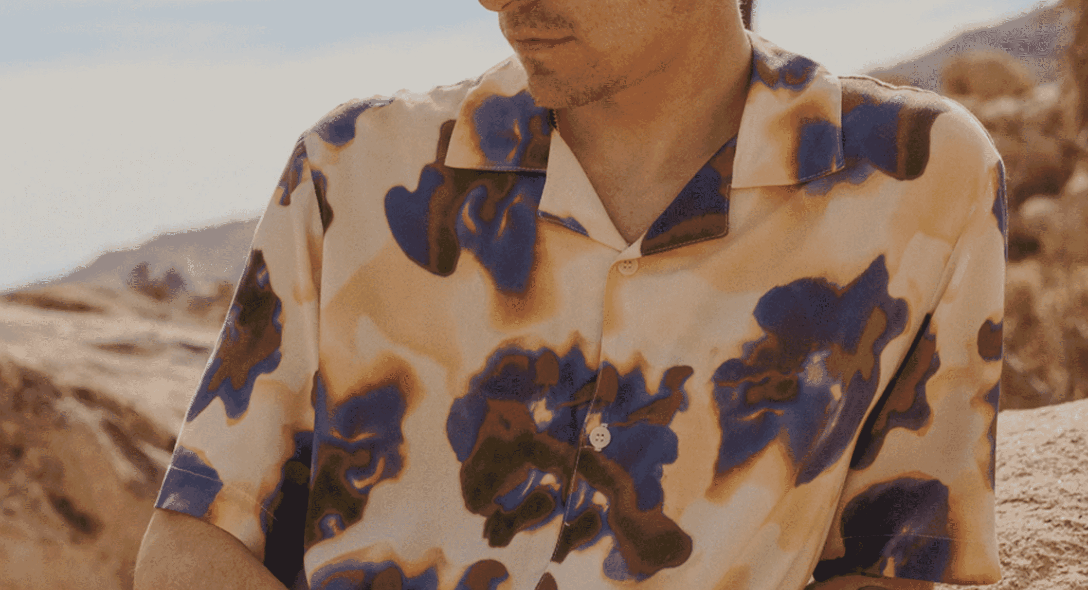 Man in a blue and brown abstract camouflage patterned shirt against a desert backdrop.